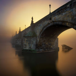 Arch bridge over river during sunset