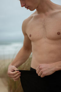 Midsection of shirtless man standing outdoors