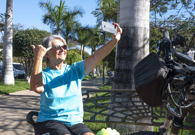 Smiling senior woman taking selfie while sitting at park