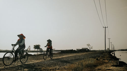 People riding bicycle on field against clear sky