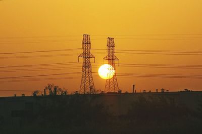 Silhouette electricity pylon against orange sky