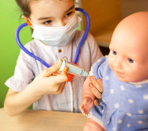 Girl imitating doctor while injecting doll at home