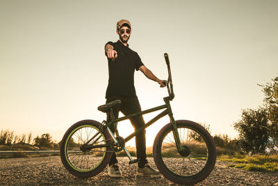 Portrait of young man riding bicycle against sky during sunset