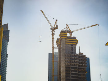 Low angle view of crane by building against clear sky