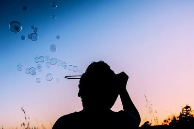 Silhouette boy blowing bubbles against sky during sunset