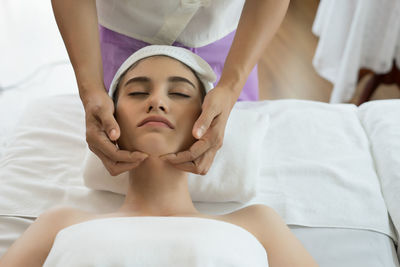 Cropped hands of massage therapist massaging young woman face in spa