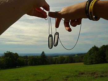 Hand holding plant by land against sky