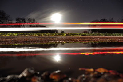 Light trails by lake against sky at night