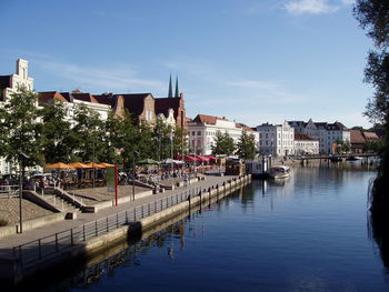 Canal by buildings in city against sky