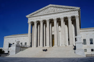 Low angle view of historical building with persons wearing blask dressed sit on stairs