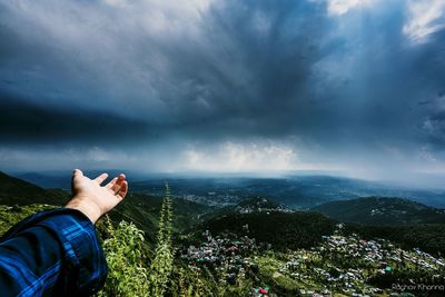 Cropped hand of man against landscape and stormy clouds