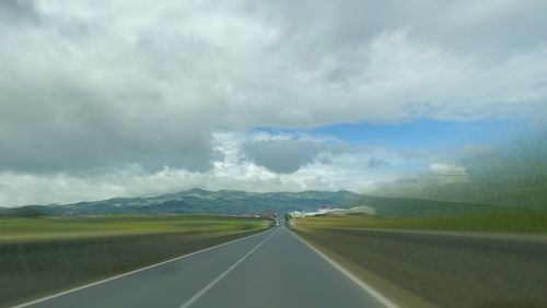 Road passing through landscape against cloudy sky