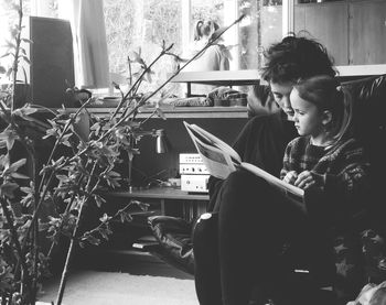 Mother and daughter reading book on chair at home