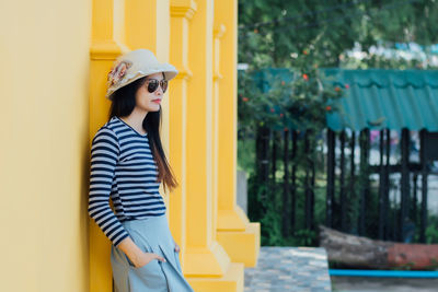 Side view of woman leaning on wall outdoors