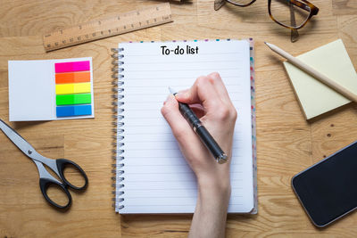 Cropped hand holding pen over spiral notebook with to do list text on table