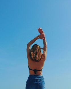 Rear view of woman standing with arms raised against clear blue sky