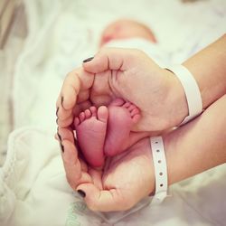 Cropped hands of woman holding baby feet in bed