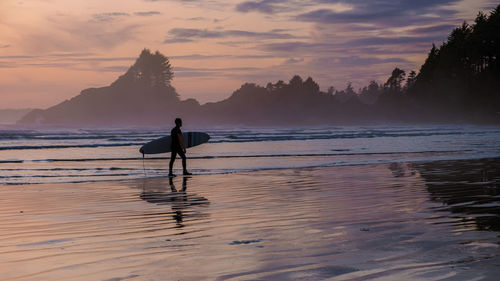 Silhouette man walking at beach against sky during sunset