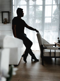 Full length of man sitting by chair at home