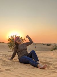 Full length of young woman at beach against sky during sunset