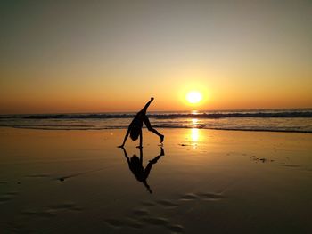 Silhouette kid doing a headstand on beach against sky during sunset