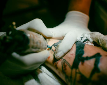 Cropped image of artist making tattoo of person hand