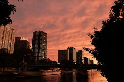 Silhouette buildings by river against sky during sunset