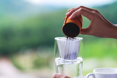 Closeup image of a hand pouring coffee grounds from grinder into a drip coffee filter