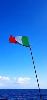 Scenic view of flag on sea against blue sky