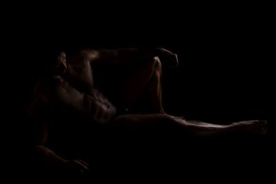 Midsection of shirtless man sitting against black background