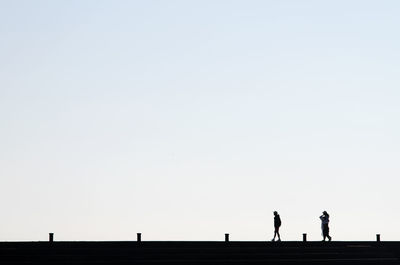 Silhouette people walking on bridge against clear sky