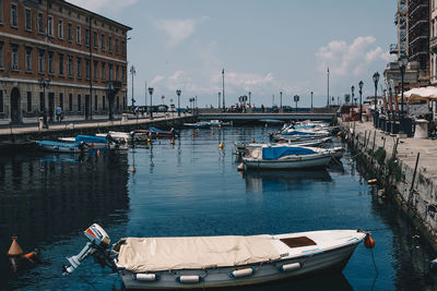 Boats moored in canal by city against sky