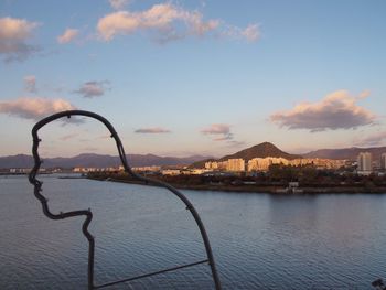 Sea by cityscape against sky during sunset