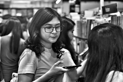 Woman with eyeglass looking for books  with cellphone on her hand