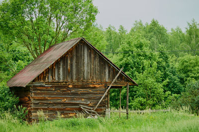 Wooden house on field by trees in forest