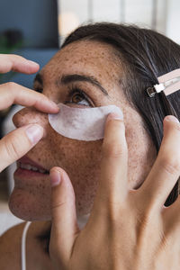 Woman applying under eye patch to friend at home