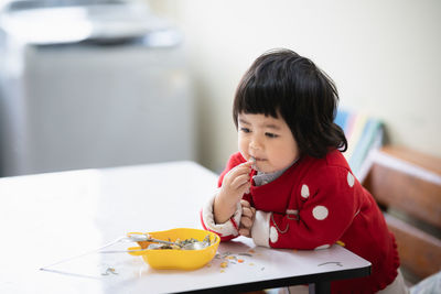 Cute girl eating food while sitting by table at home