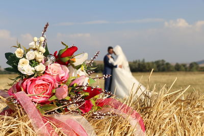 Close-up of bouquet on field with newlywed couple in background