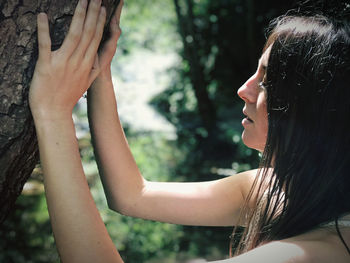 A woman rests her hands on the bark of a tree