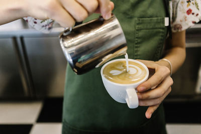 Young woman pouring milk while standing at coffee shop