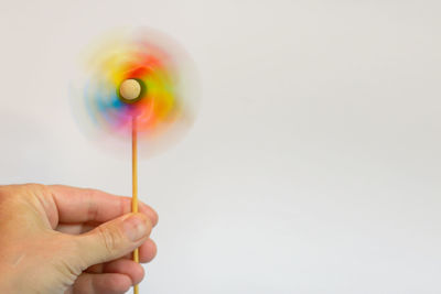 Close-up of hand holding spinning pinwheel toy over white background