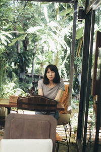 Young woman sitting on chair against plants