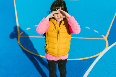 Girl shielding eyes while standing at basketball court on sunny day