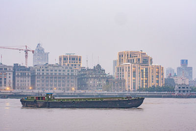 Freight boat in shanghai river. crane and buildings in background.