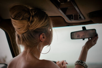 Rear view of woman holding mirror sitting in car