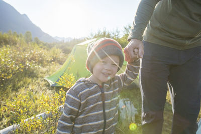 Young boy holding fathers hand while on a camping trip outdoors.