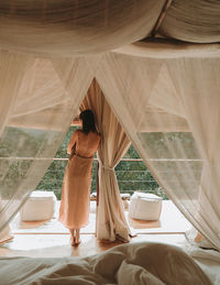 Rear view of woman standing by curtains