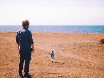 Rear view of men on beach against sky