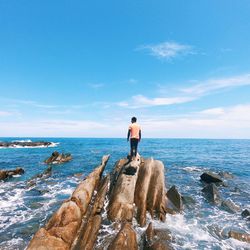 People standing on rock at beach against blue sky