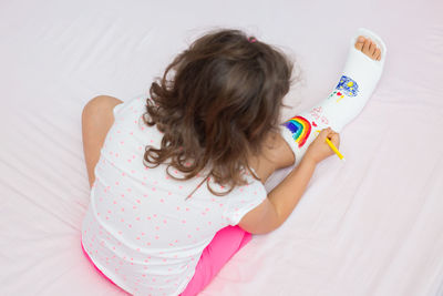 Rear view of woman with arms raised sitting on bed at home